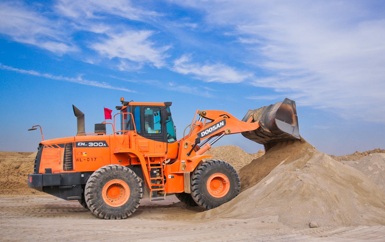 EXPERIENCIA EN OBRAS CIVILES INSTITUCIONES PÚBLICAS An orange bulldozer at work, moving sand under a clear blue sky on a construction site.
