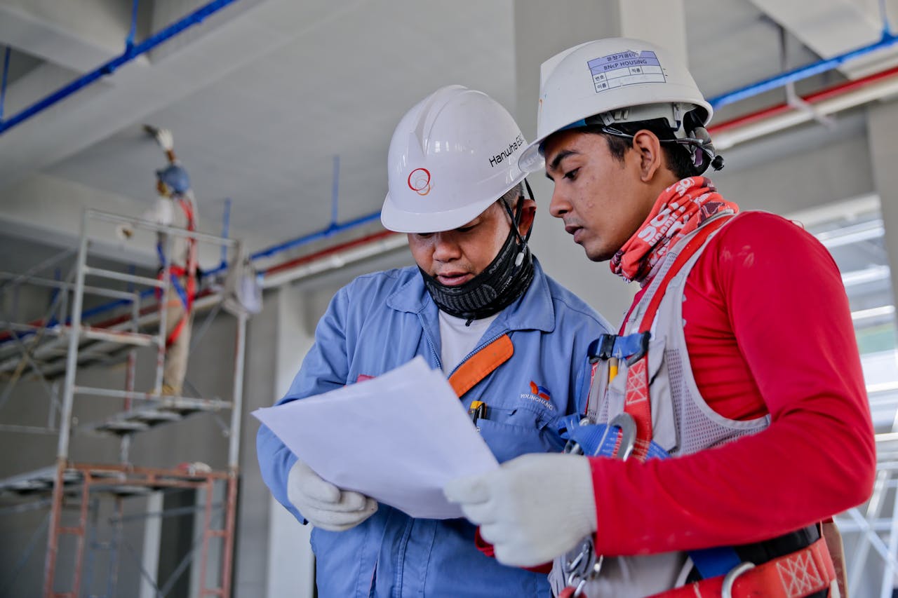 CURSOS Y SEMINARIOS Two engineers in safety helmets reviewing construction plans at a worksite.