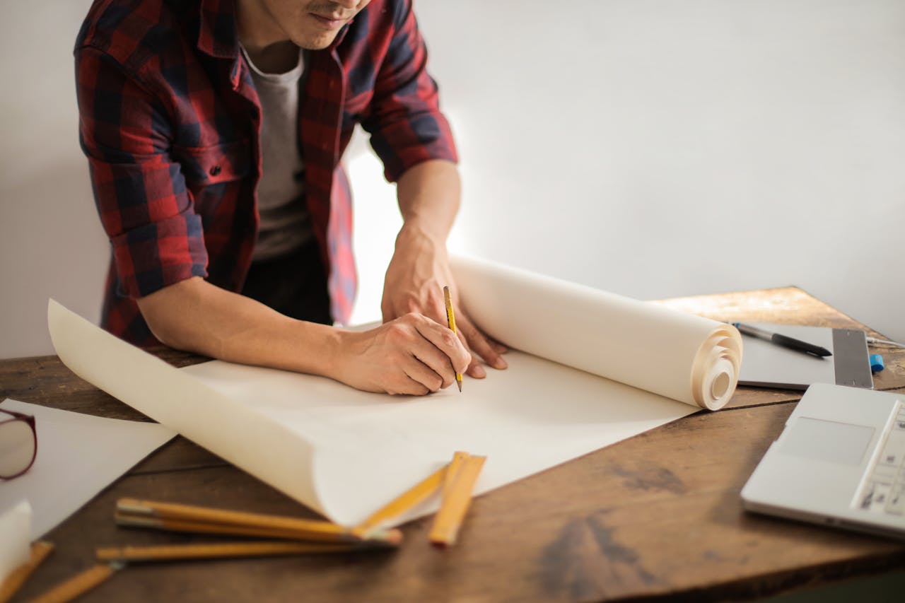 ESTUDIOS DE POS – GRADO A focused architectural designer drafting blueprints at a desk indoors.
